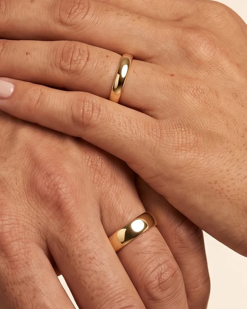 Las manos de una pareja, cada una con su argolla de matrimonio de oro