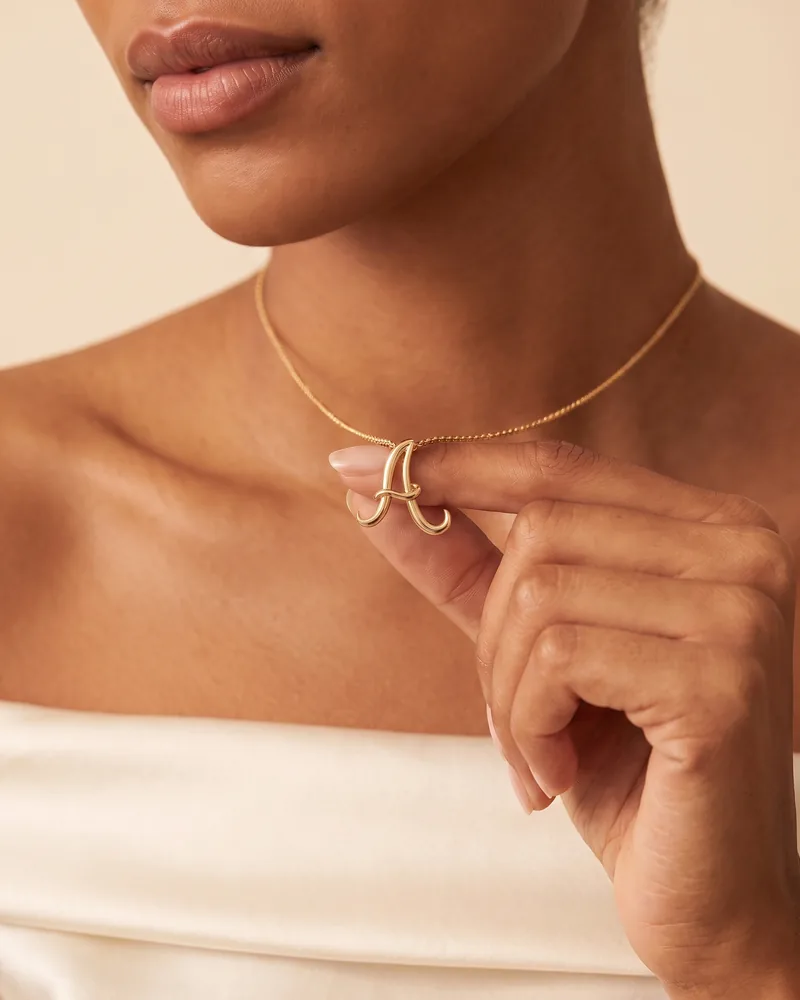 Mujer que sostiene entre los dedos su dije de inicial "A" cursiva en oro amarillo