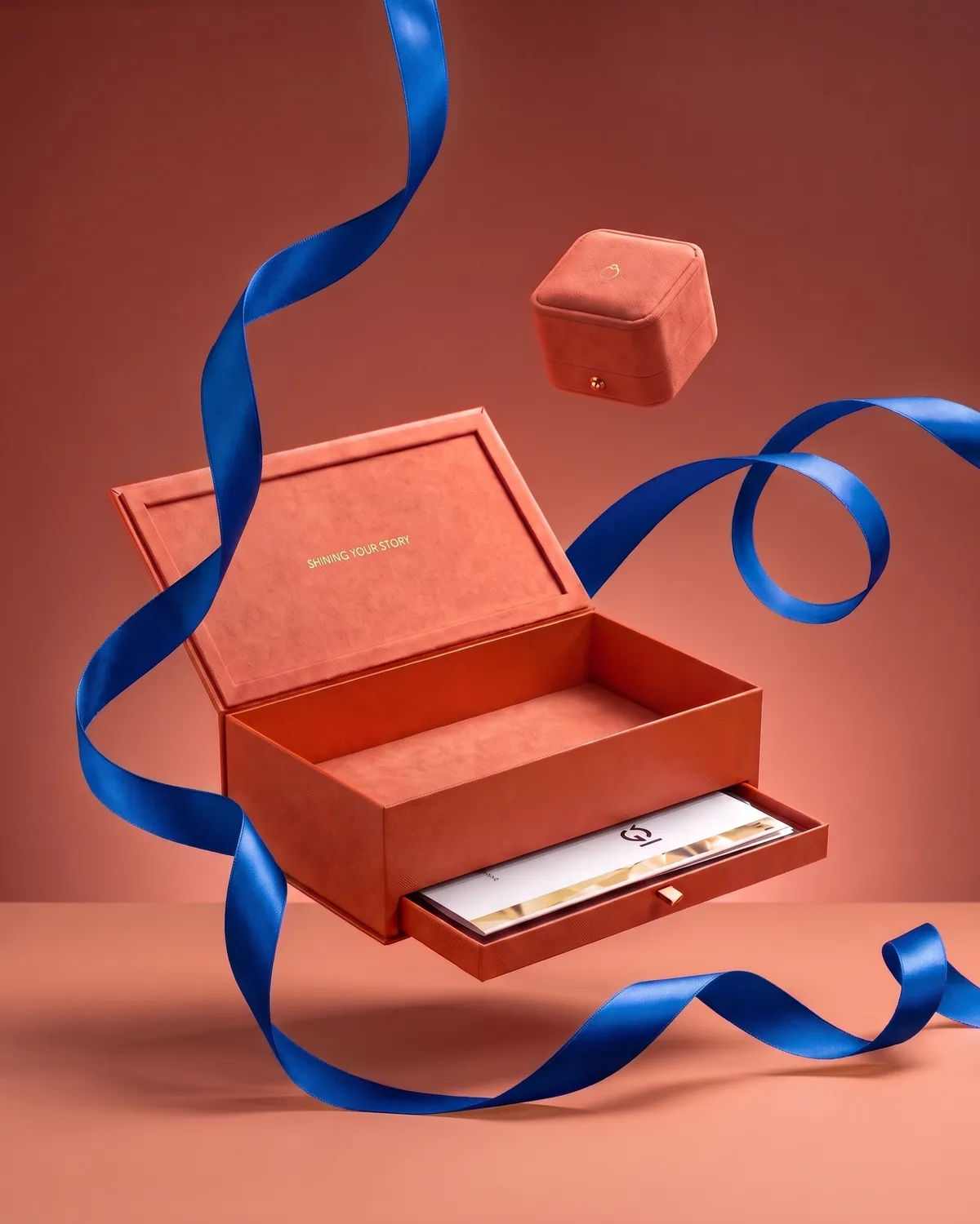 Caja de presentación Matrimony coral con su cajón y el certificado, junto al estuche cerrado con el isologo dorado y un listón azul rey