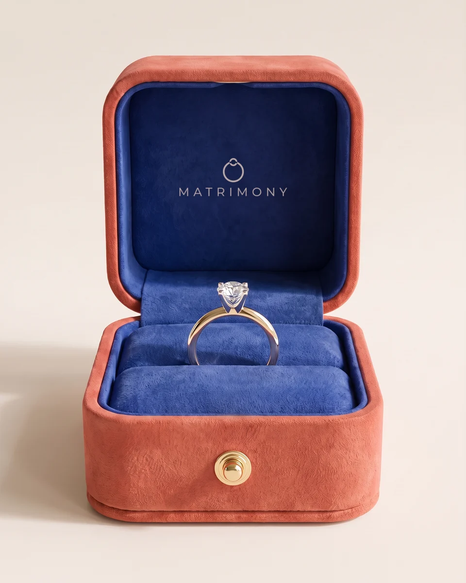 Estuche Matrimony de gamuza coral abierto, con terciopelo azul rey y un anillo de compromiso de oro amarillo