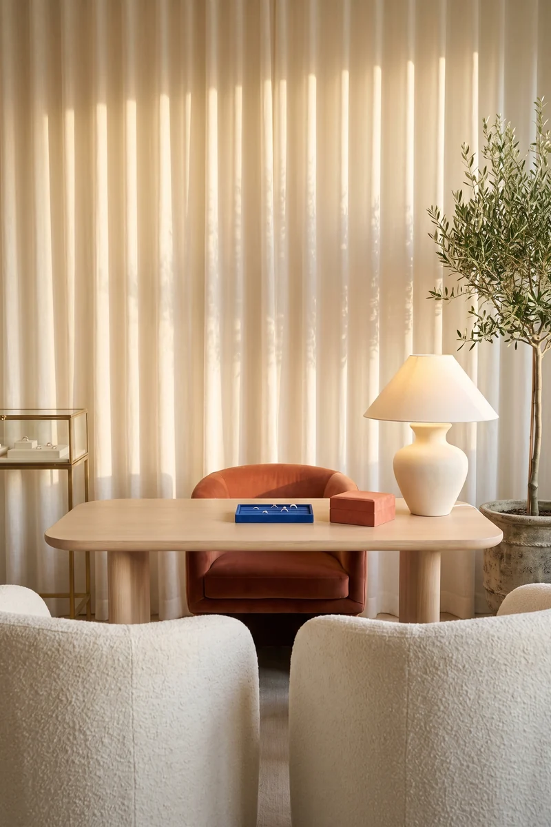 Sala de asesoría privada con cortinas de lino, mesa de roble claro, sillón terracota y una charola de anillos
